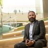 Temple University alum Christopher Barnett, class of 2010, wearing a suit and sitting on the steps at the new Paley Hall on Main Campus